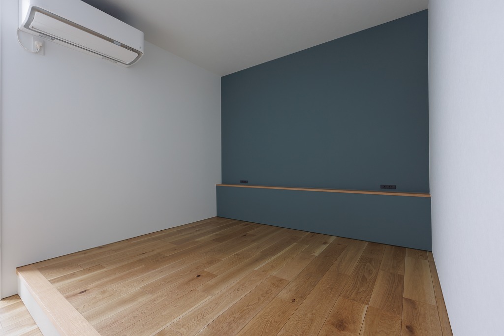 ブルーグレーのアクセントクロスが映える、小上がりのあるモダン寝室